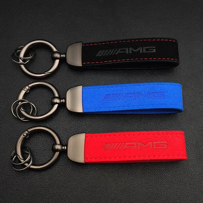 Three AMG branded keychains in black, blue, and red on a dark surface.